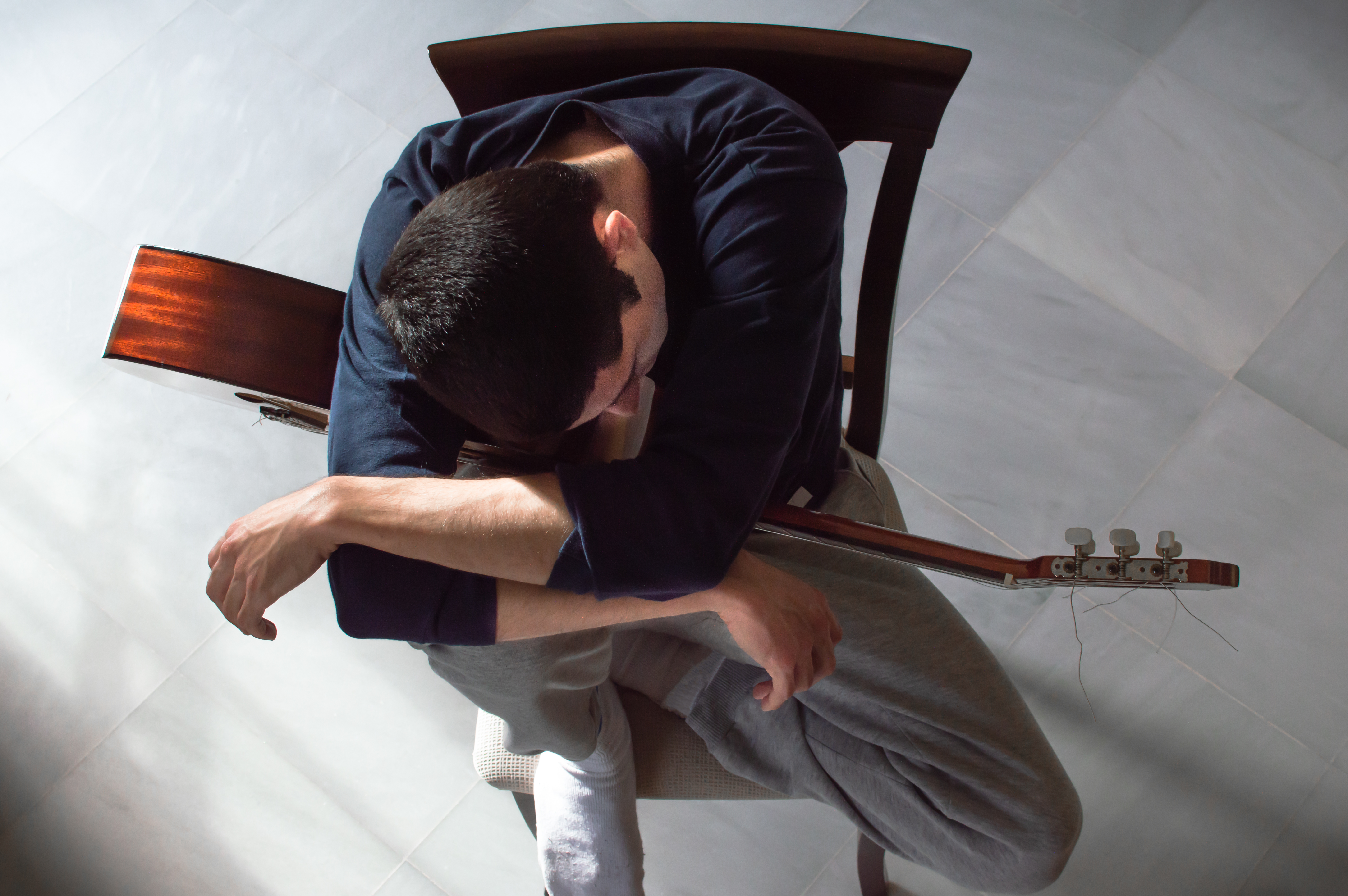 Man sitting with Guitar looking sad.