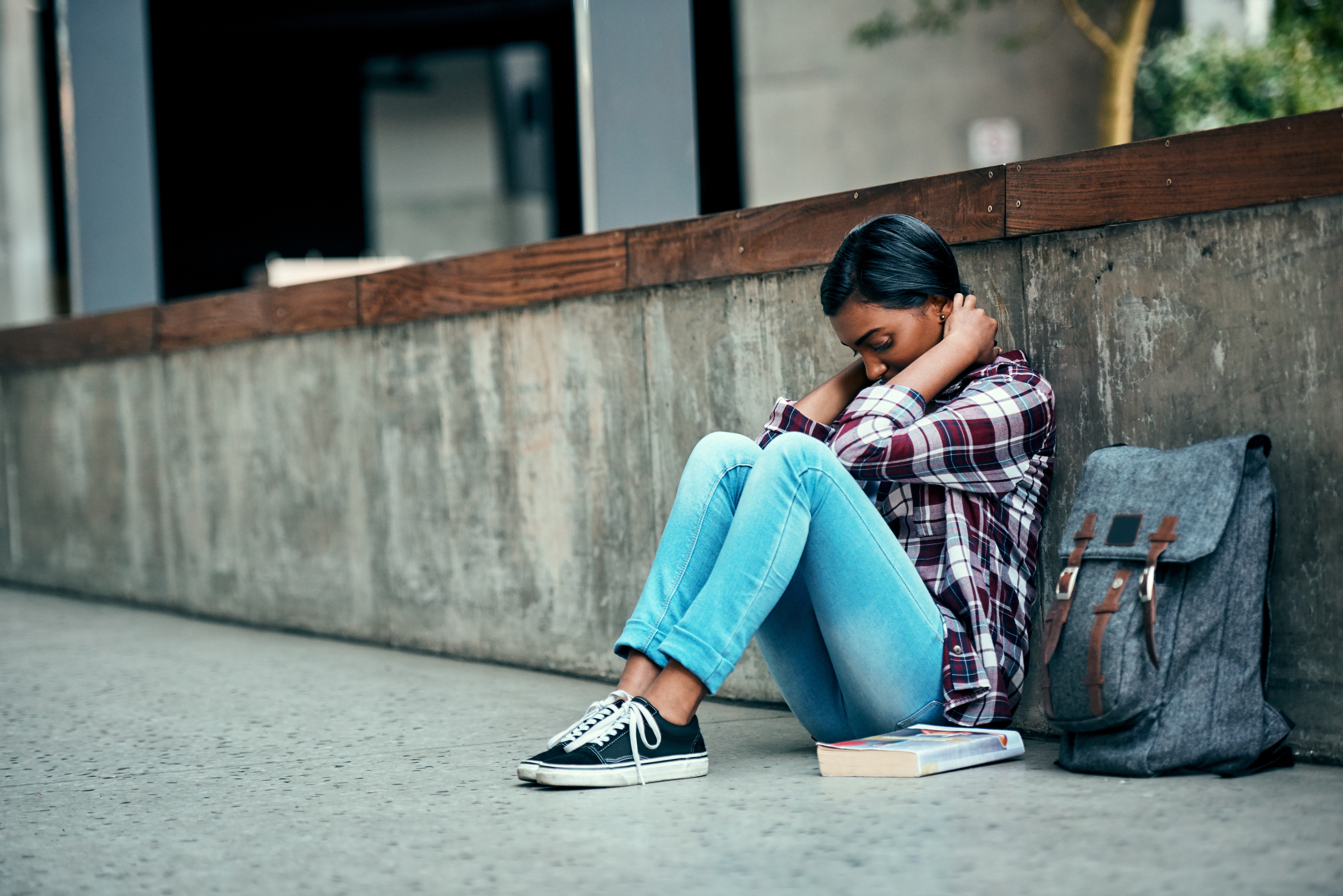 Student sitting on sidewalk looking sad.