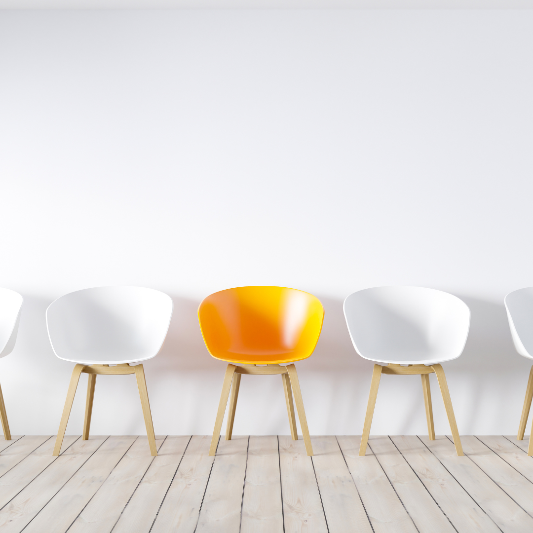 A row of white chairs in an otherwise empty room with one yellow one in the middle. 