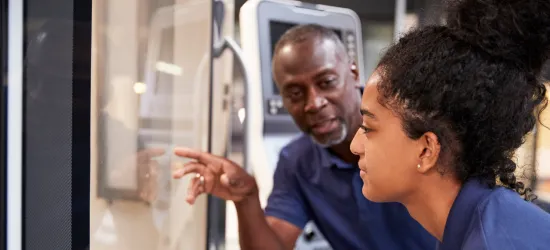 Photo of a mentor teaching a young woman about a machine during job training