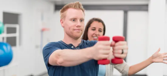 Photo of a young woman volunteering in a VA clinic with a veteran in physical therapy