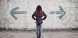 Girl facing wall that has two arrows spray painted on it pointing in opposite directions