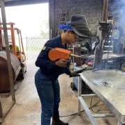 Karina is welding a metal piece on a bench