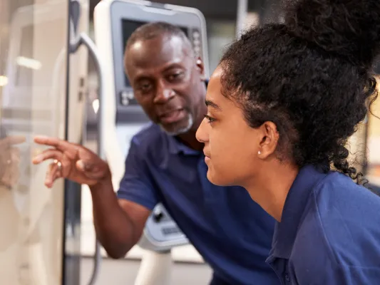 Photo of a mentor teaching a young woman about a machine during job training