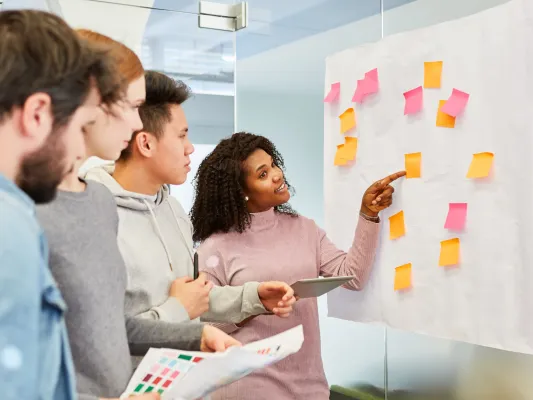 Group of young workers looking at a white board with sticky notes