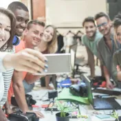 Photo of eight young people taking a selfie at a desk where they are working